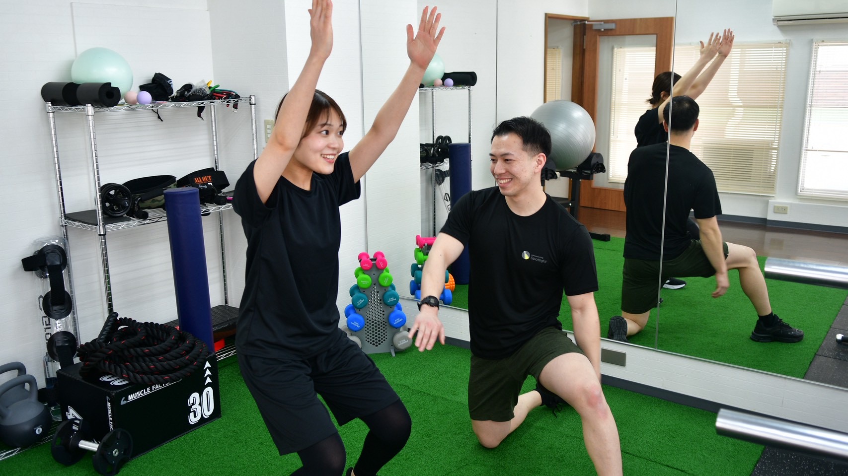 トレーナーと一緒に笑顔で体を動かす女性