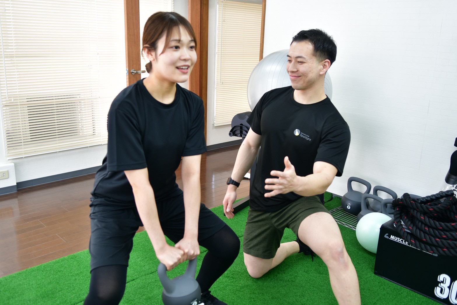 トレーナーに見守られながらケトルベルを持ち上げる女性